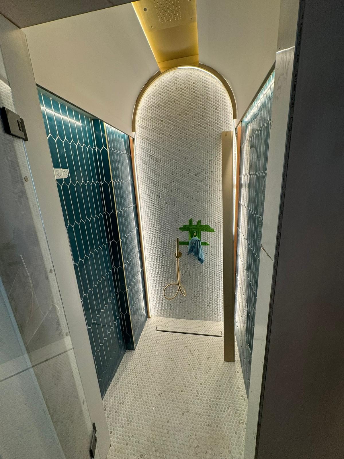 Walk-in wet room with teal hex tile and brass rain shower